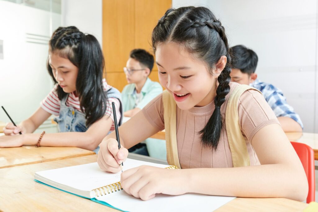 Children smiling and writing in classroom during Holiday English Club for Kids at ILC Hua Hin