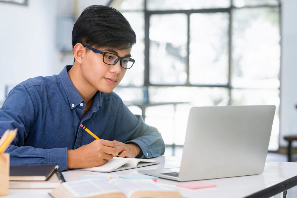 Student preparing for IELTS 2025 Education Theme exam with laptop and notes in a study session