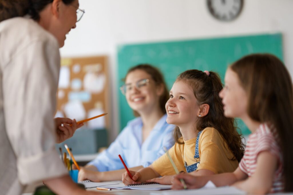 Children smiling and learning with their teacher during a Trinity English lesson in the classroom.