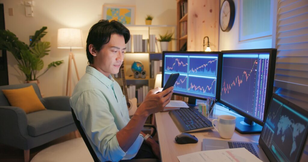 Young man studying financial charts on multiple screens at home, symbolising IELTS Economy and Trade, global markets, and consumer trends.