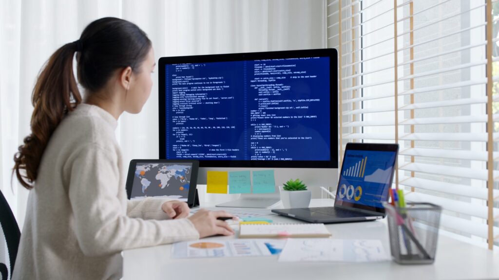 Student preparing for IELTS Work and Careers 2025 by studying computer-based tasks, coding on screen, and analysing data charts in a modern office.