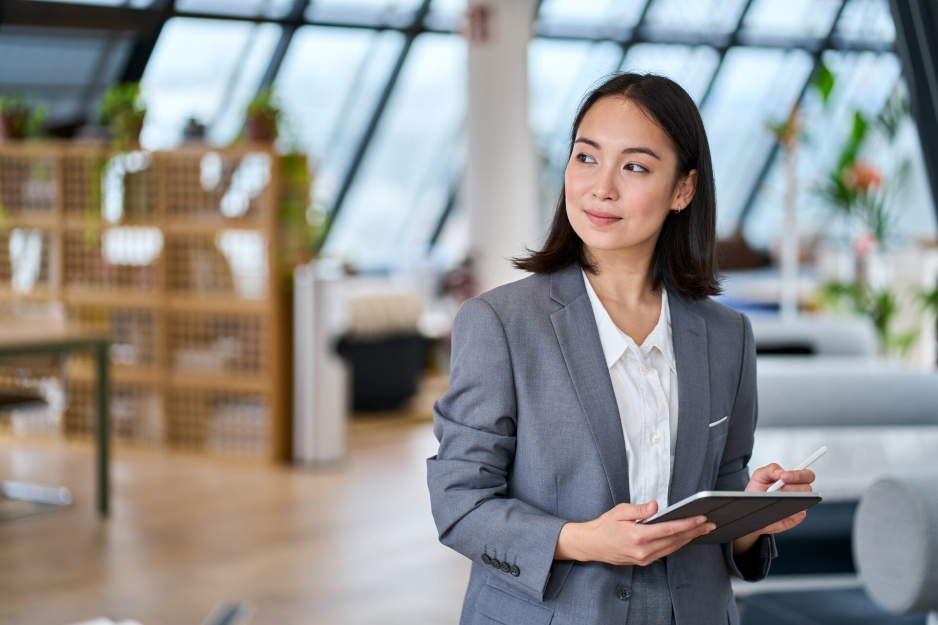 Confident young professional woman in business suit holding tablet, representing IELTS Work and Careers 2025 theme of future jobs and career success.