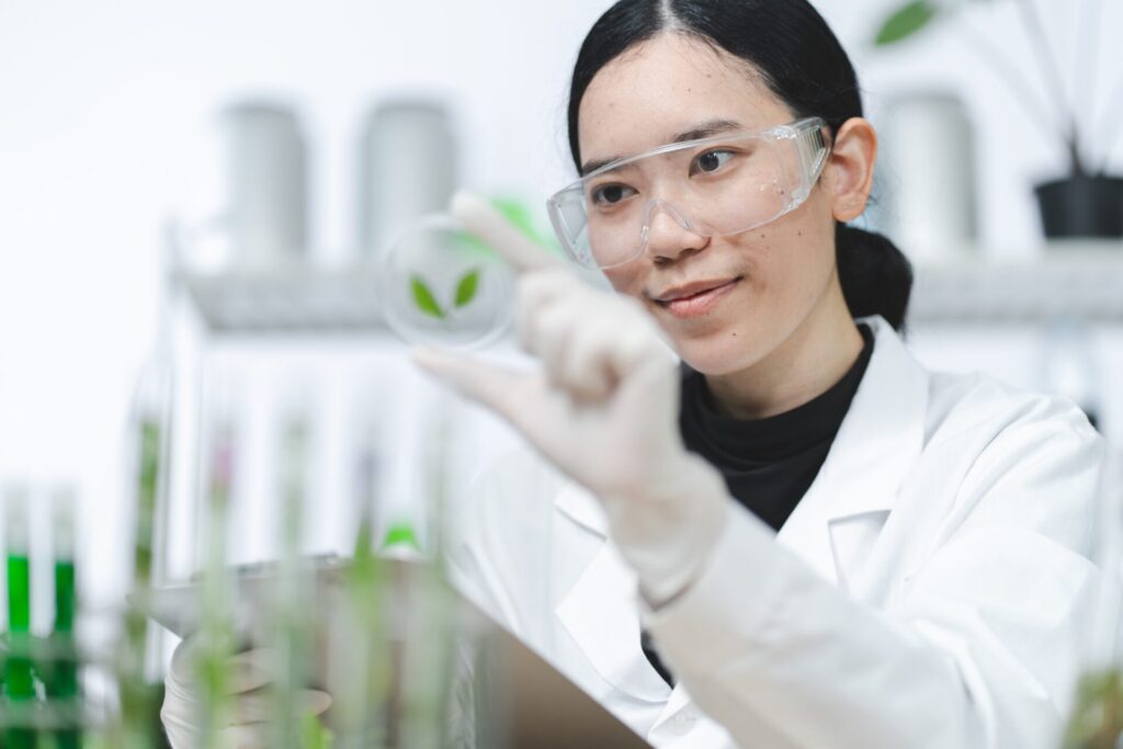 Female scientist in a laboratory examining plant leaves in a petri dish, symbolising IELTS Science and Innovation with biotechnology and research themes.