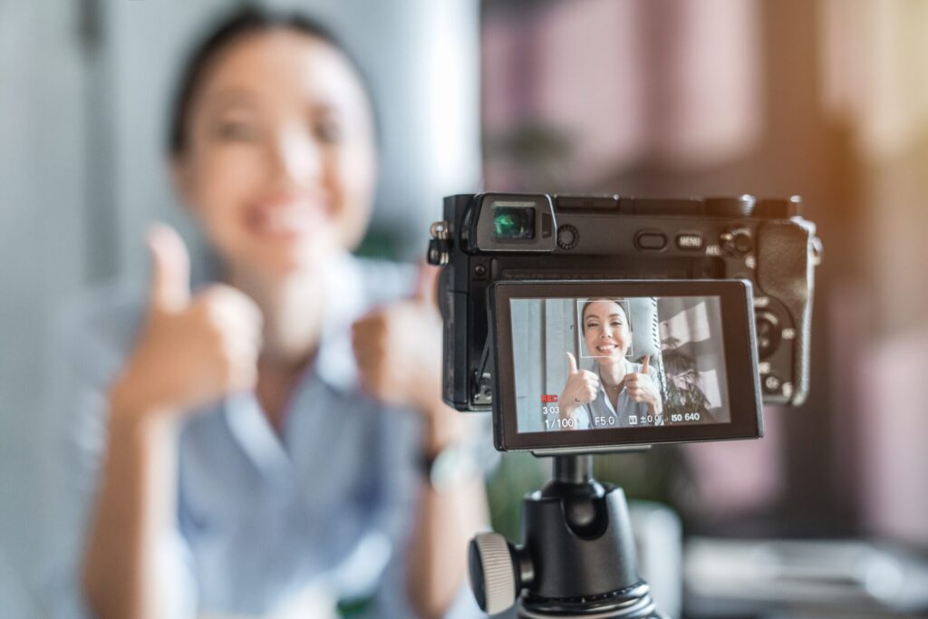 IELTS Media and Advertising example with influencer recording video content and giving thumbs up on camera.