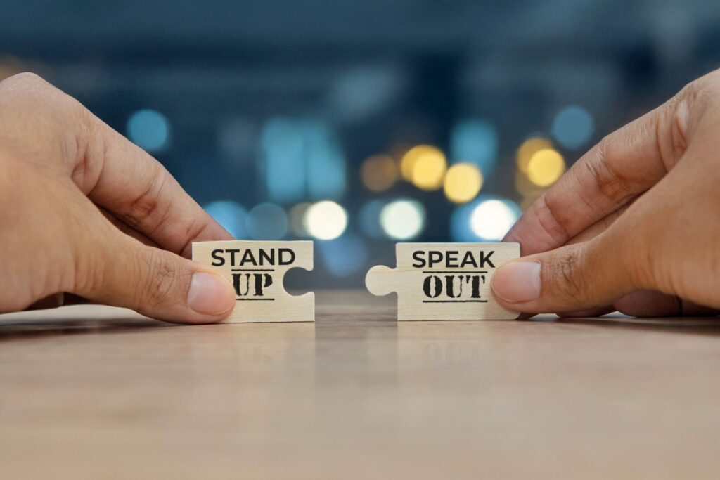 Hands holding two puzzle pieces that say “Stand Up” and “Speak Out,” symbolising IELTS Society and Inequality themes of fairness and justice.