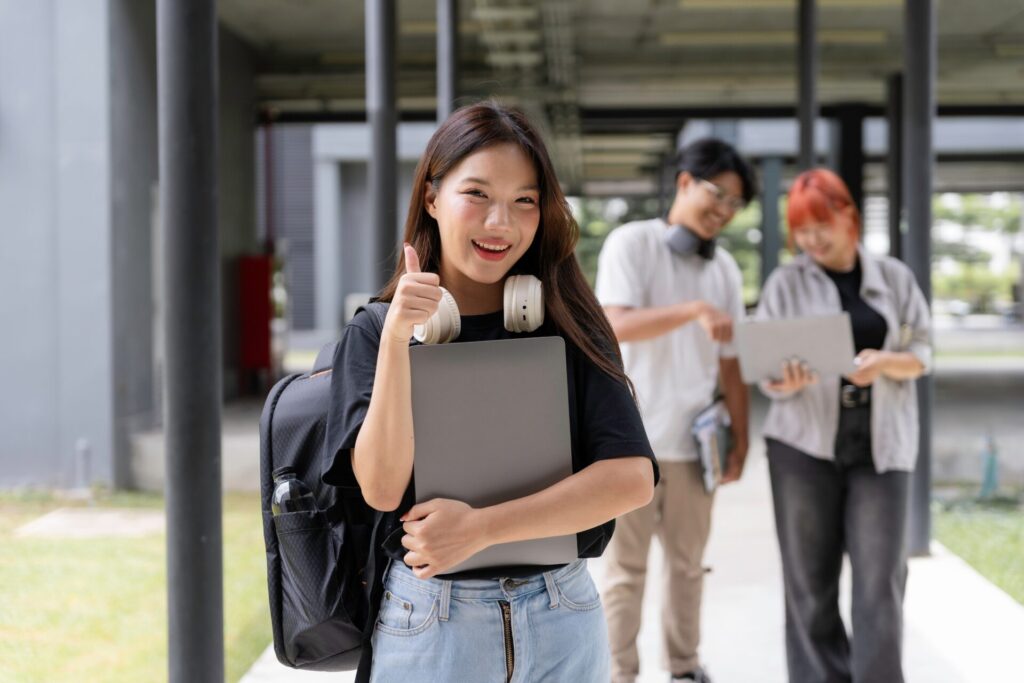 Thai student smiling and holding a laptop at ILC Hua Hin while learning English for beginners in Thailand.