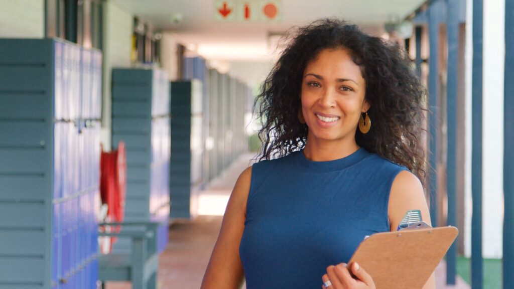 Smiling teacher holding a clipboard in a bright hallway – helping students learn English in Hua Hin