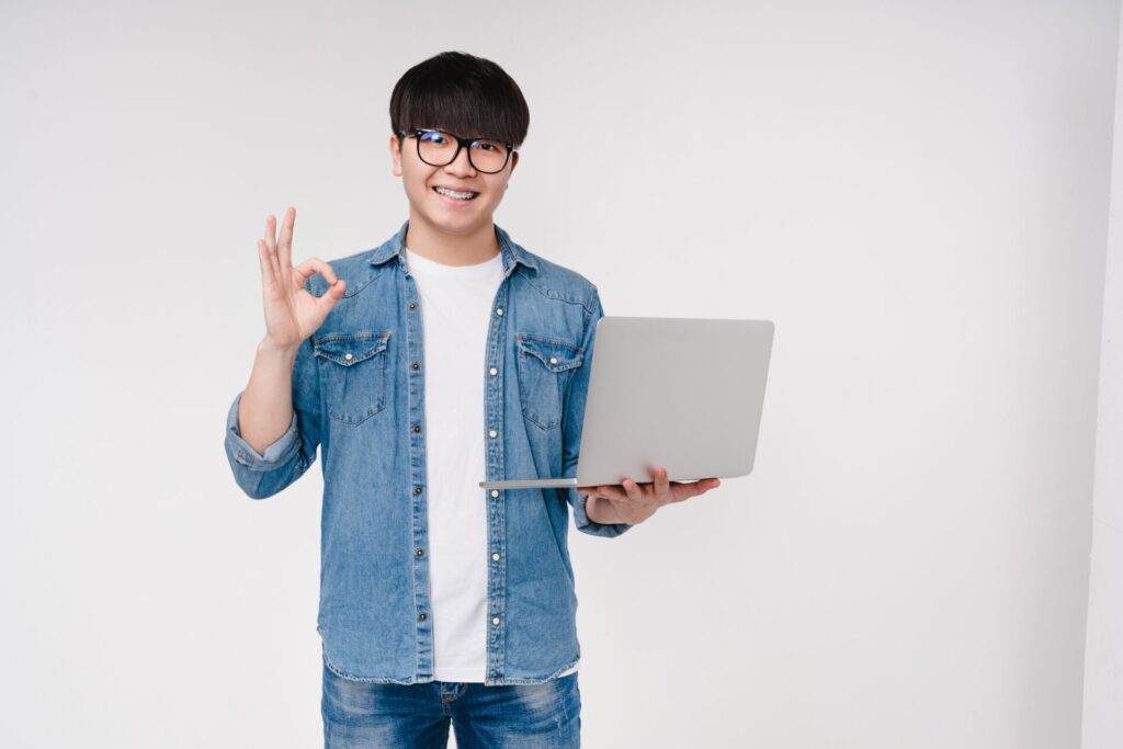 Smiling student holding a laptop and giving an OK gesture during English classes in Hua Hin