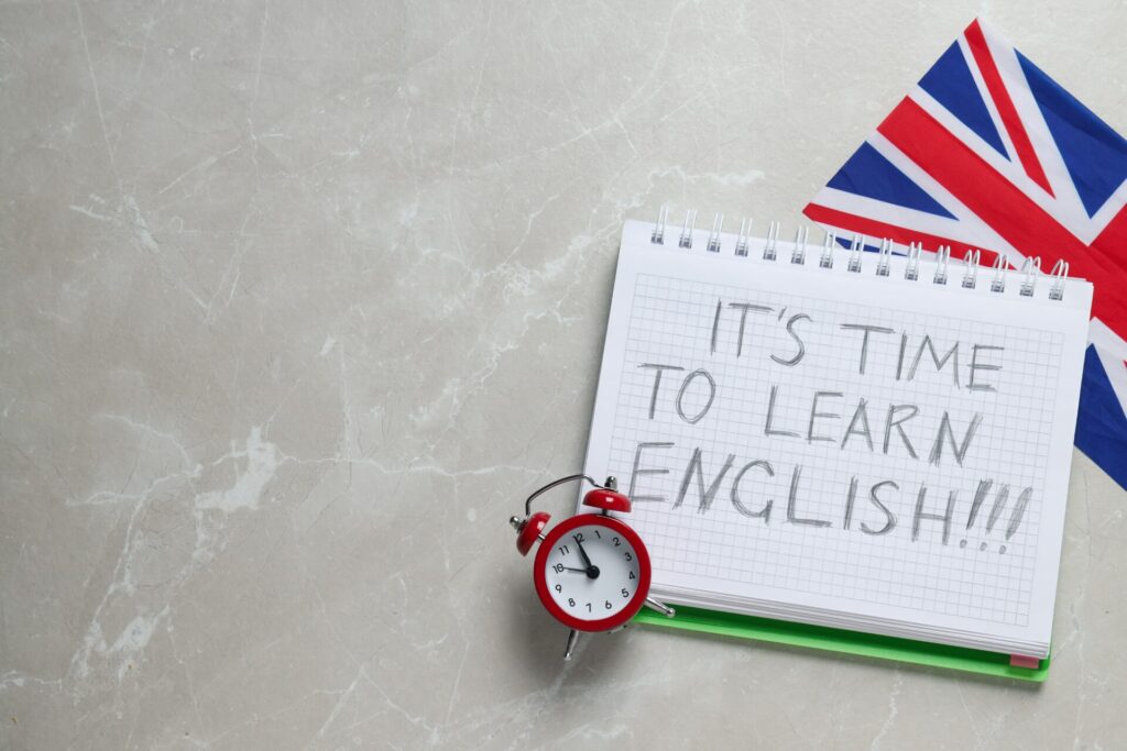 Beginner English Coaching 1 Beginner English coaching reminder with notepad, British flag, and clock on a desk