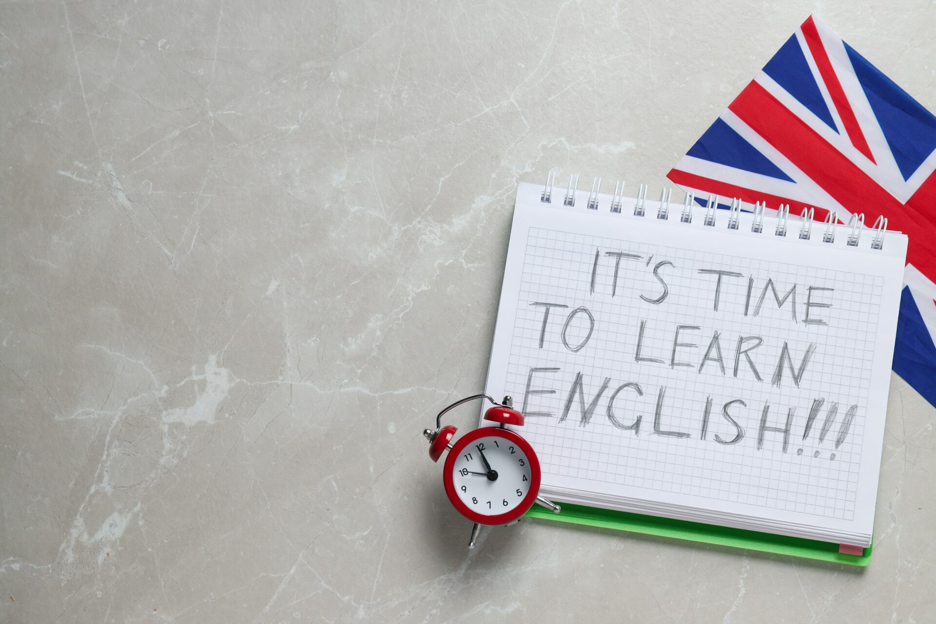 Beginner English coaching reminder with notepad, British flag, and clock on a desk