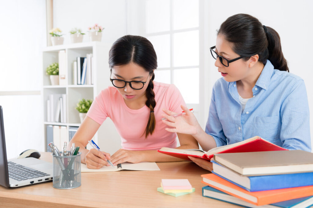 Student receiving one-to-one English coaching with a teacher explaining grammar during GESE 1 preparation to help her learn to speak English quickly.